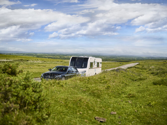 A car towing a caravan in the countryside surrounded by open fields. Discover second hand caravans for sale at Webbs. New Caravan Towing Rules by Webbs.