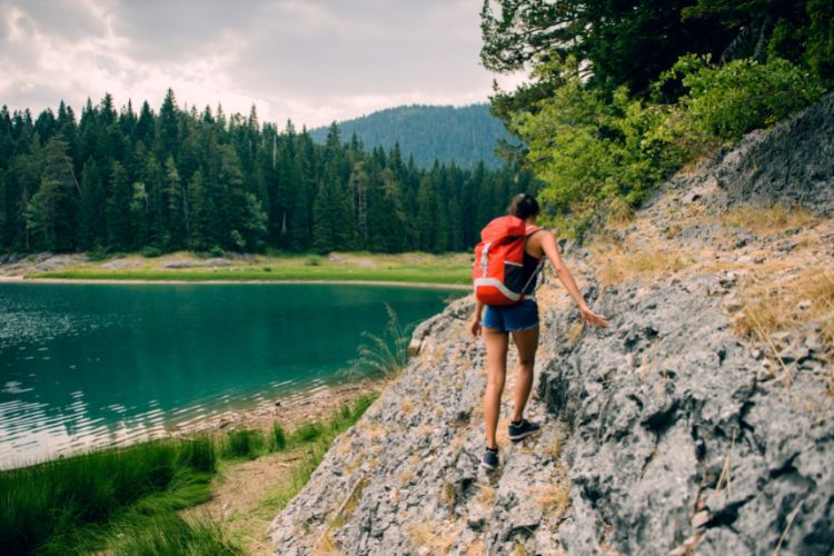 Female camper scaling the a small rockface next to lake. 5 Reasons Why Camping Is Good For You by Webbs.