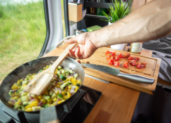 A person cooking a meal in a caravan or motorhome. Tips and ideas from Webbs for embracing off-season weather in your motorhome, caravan or camping travels.