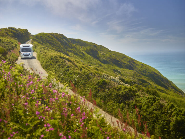 A Bailey motorhome driving along a track on a cliff by the sea. Bailey of Bristol Brand Showcase by Webbs.