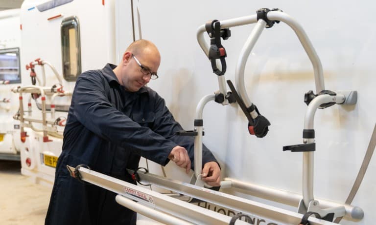 A member of the service team bolting on a bike rack to a used motorhome at Webbs, a motorhome dealer.