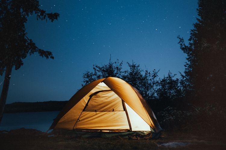 A tent lit up at night under a clear sky. 5 Reasons Why Camping Is Good For You by Webbs.
