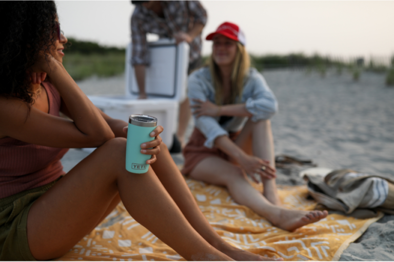 Two girls sat on a beach drinking from a YETI tumblr, from Webbs Outdoors
