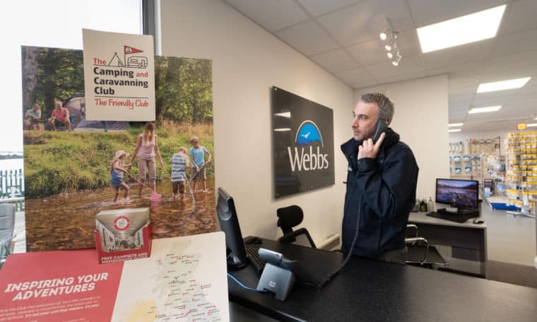 A Webbs member of staff on the phone next to the Camping and Caravanning Club sign.