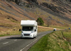 A motorhome travelling along a road by some hills or mountains. Tips and ideas from Webbs for embracing off-season weather in your motorhome, caravan or camping travels.