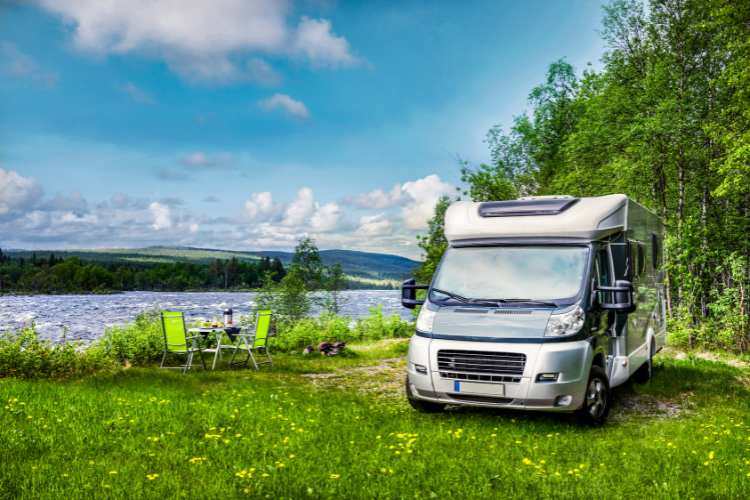 A motorhome parked on grass next to a large lake with trees behind. A Webbs blog on ensuring safety and security in your motorhome or caravan adventure.