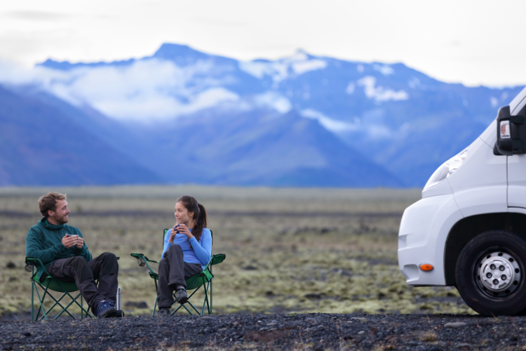 A couple enjoying a cup of tea by their motorhome with mountains in the background. Touring Routes to Explore in the UK by Webbs.