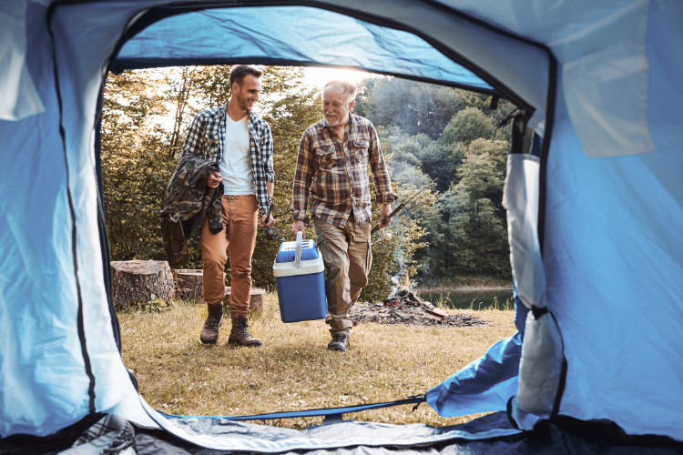 Two men heading back to their tent carrying a cool box. Summer survival tips in your caravan or motorhome by Webbs.