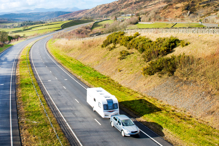 A caravan being towed through the countryside in Wales. Touring Routes to Explore in the UK by Webbs.