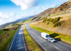 A caravan driving on the open road, surrounded by fields and hills.