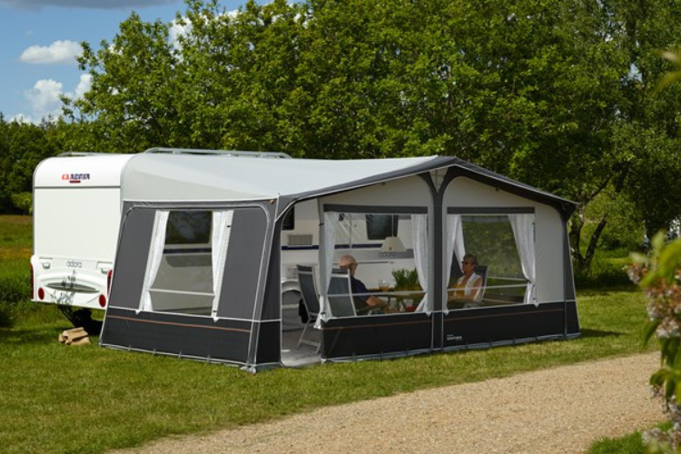 Caravan with an awning attached and people a couple sat in the awning. Summer survival tips in your caravan or motorhome by Webbs.