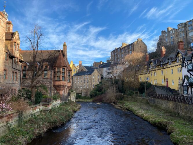 A river running through a series of houses and buildings in a Scottish town. How To Plan Your Perfect Motorhome Getaway by Webbs.