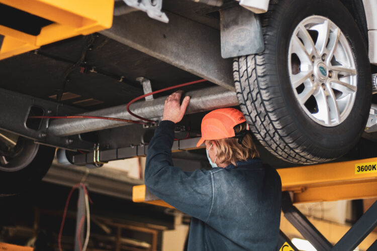 A Webbs Workshop worker under a van in the workshop. Top 5 tips for new caravan owners blog by Webbs.